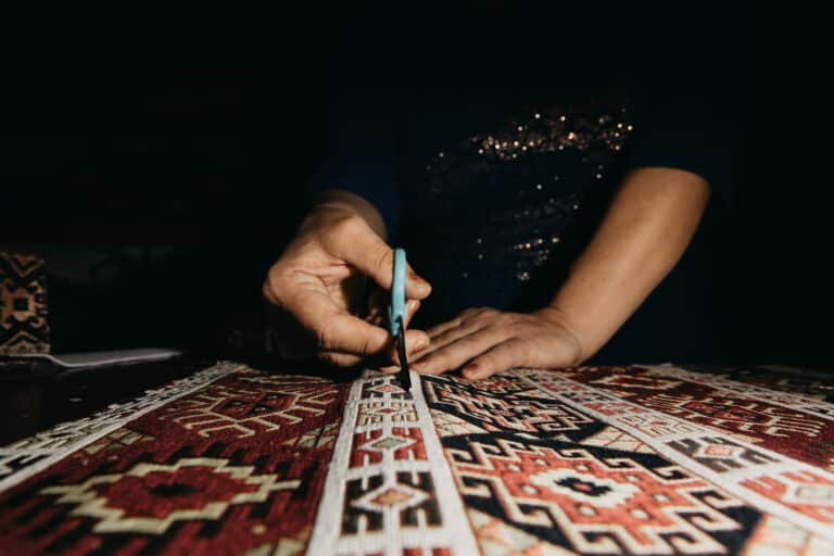 Mains d'artisan travaillant à la cisaille sur un tapis ancien à motifs