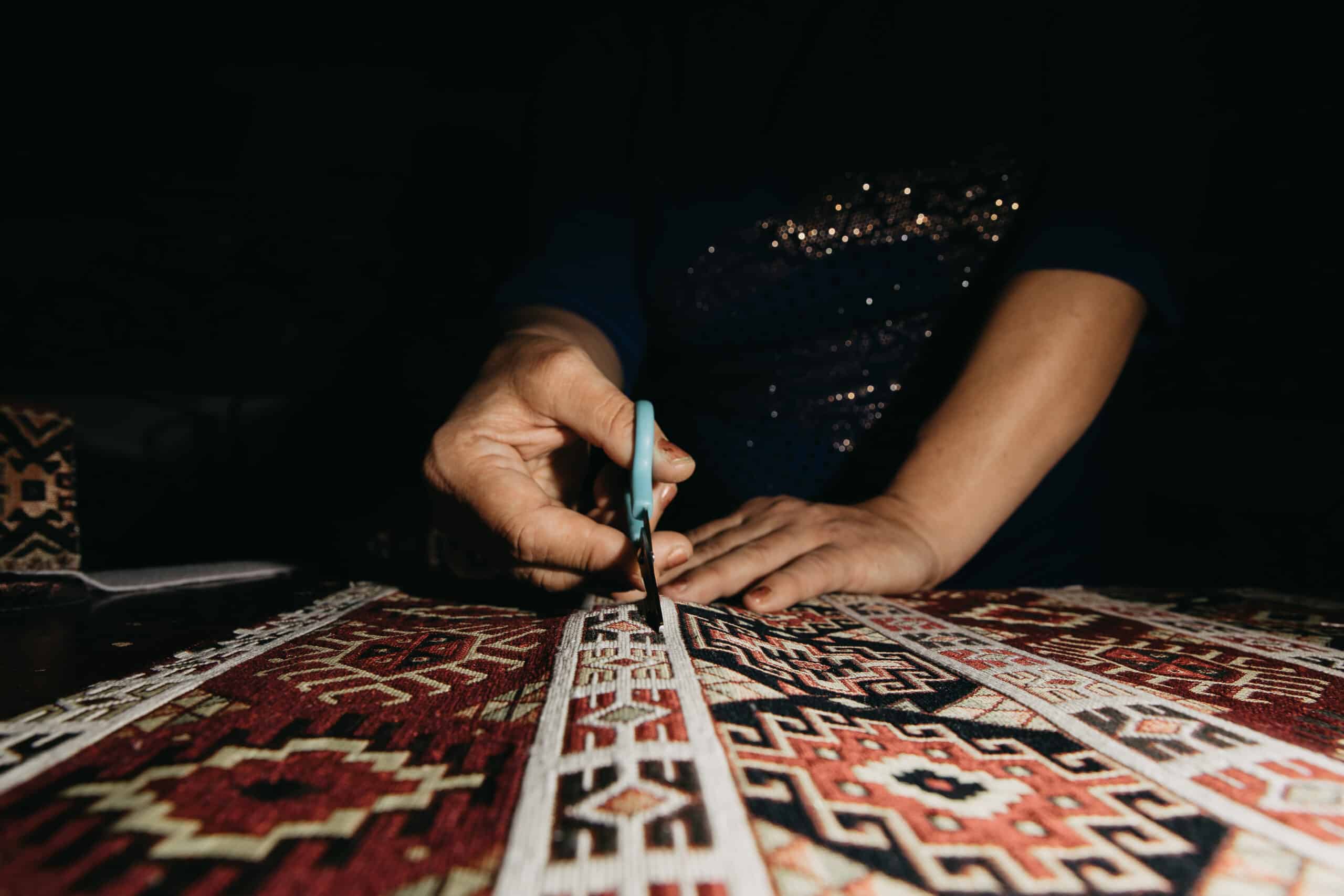 Mains d'artisan travaillant à la cisaille sur un tapis ancien à motifs