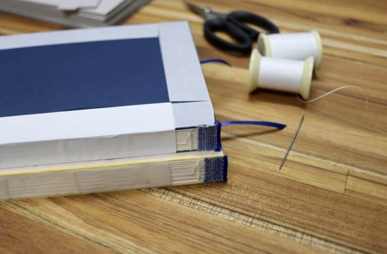 Livres en cours de reliure avec fil, aiguille et ciseaux sur l'établi d'un atelier