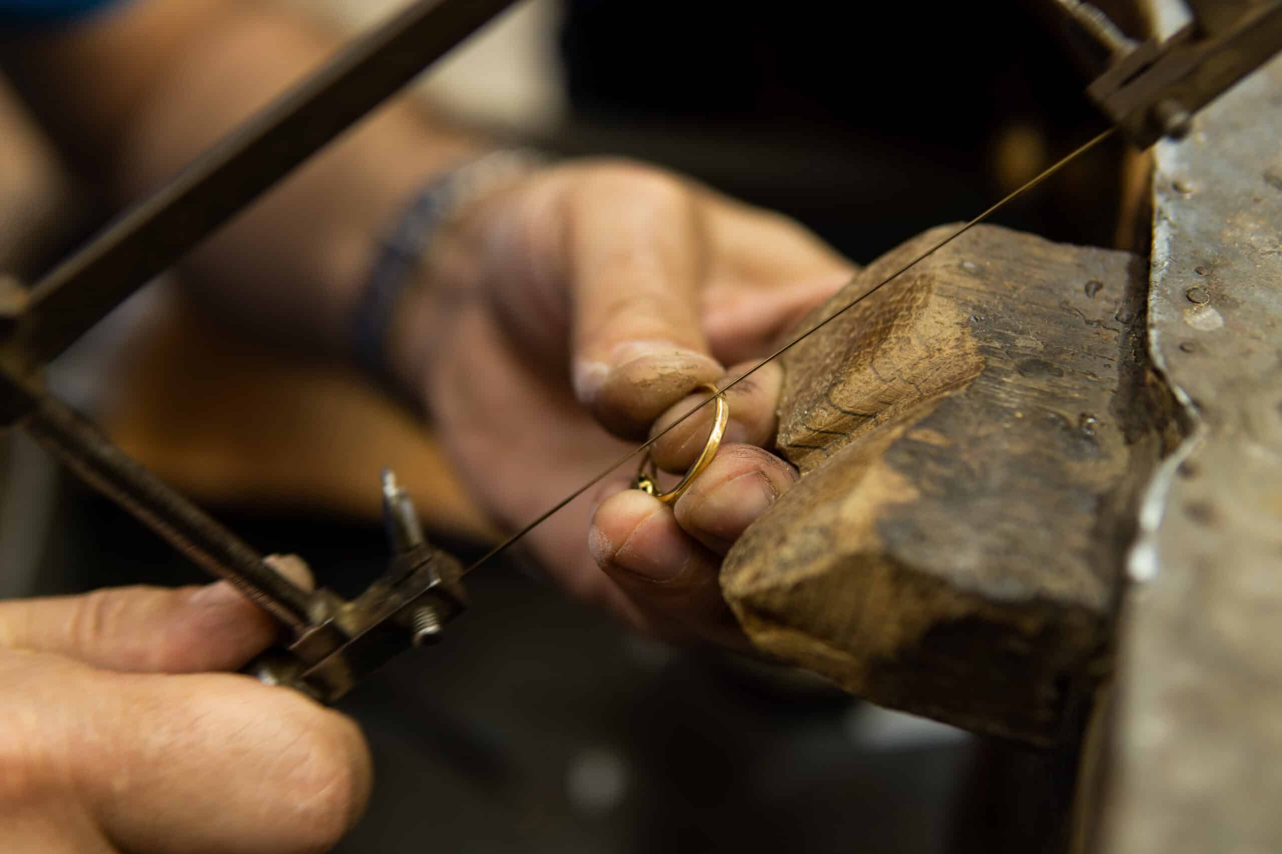 Mains d'un bijoutier sciant une bague en or sur la cheville de son établi